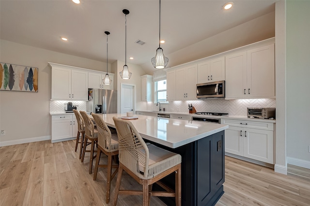 kitchen featuring a kitchen island, white cabinetry, hanging light fixtures, and appliances with stainless steel finishes