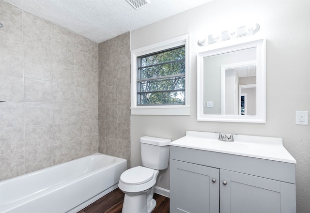 full bathroom with vanity, hardwood / wood-style flooring, tiled shower / bath combo, toilet, and a textured ceiling