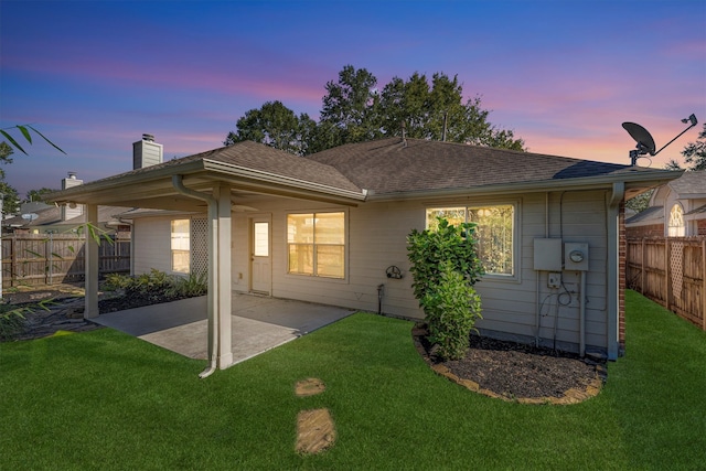 back house at dusk with a patio area and a yard