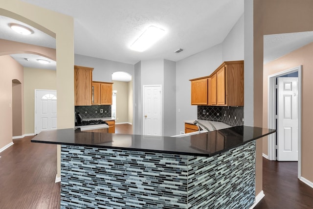 kitchen with kitchen peninsula, a textured ceiling, tasteful backsplash, and dark hardwood / wood-style floors