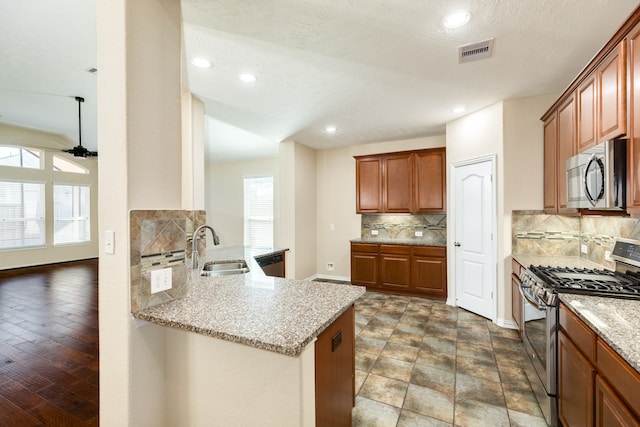 kitchen with kitchen peninsula, appliances with stainless steel finishes, tasteful backsplash, dark wood-type flooring, and sink