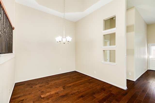 spare room featuring dark hardwood / wood-style flooring, an inviting chandelier, and built in features