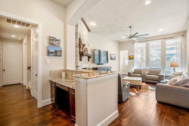 kitchen featuring ceiling fan, light stone countertops, dark wood-type flooring, and kitchen peninsula