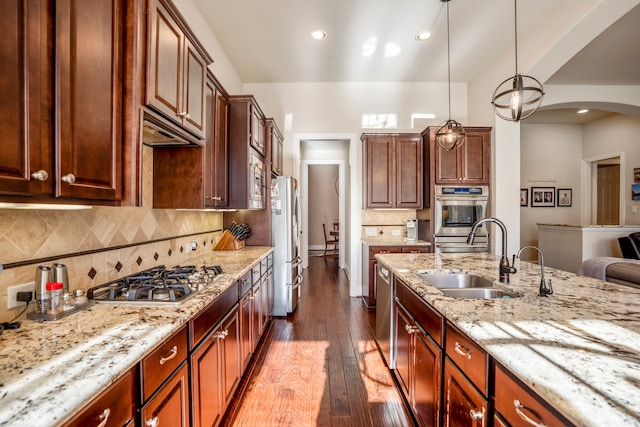 kitchen featuring hardwood / wood-style floors, sink, hanging light fixtures, light stone countertops, and stainless steel appliances