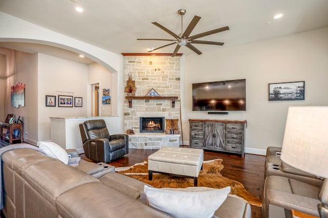 living room featuring dark hardwood / wood-style floors, a stone fireplace, and ceiling fan