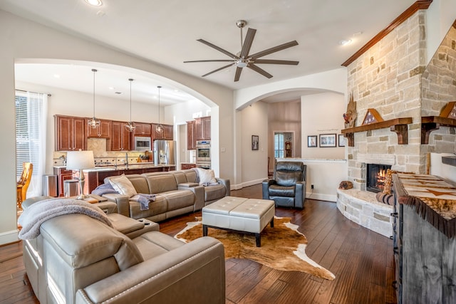 living room featuring ceiling fan, a stone fireplace, dark hardwood / wood-style flooring, and plenty of natural light