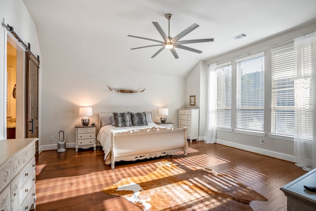 bedroom with ceiling fan, a barn door, dark hardwood / wood-style floors, and vaulted ceiling