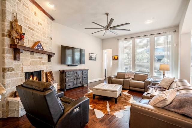 living room featuring a stone fireplace, ceiling fan, and dark wood-type flooring