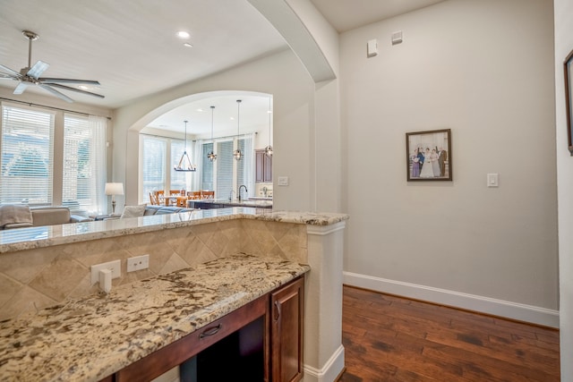 kitchen featuring light stone counters, dark hardwood / wood-style flooring, ceiling fan, and hanging light fixtures