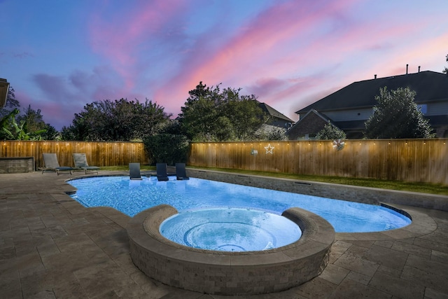 pool at dusk featuring an in ground hot tub and a patio