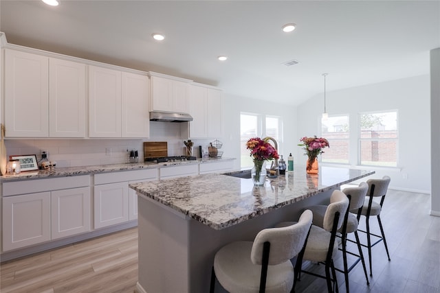 kitchen featuring a wealth of natural light, white cabinets, and an island with sink