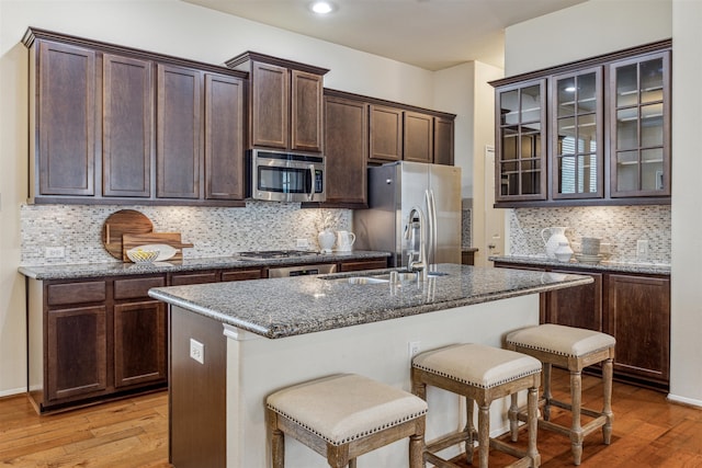 kitchen with a center island with sink, stone counters, light hardwood / wood-style floors, and appliances with stainless steel finishes