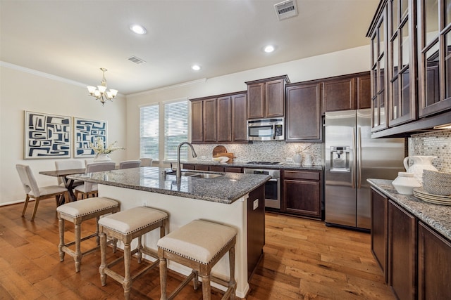 kitchen featuring light wood-type flooring, stainless steel appliances, dark stone counters, and sink