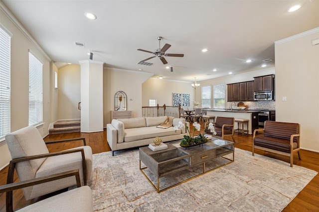 living room featuring ceiling fan with notable chandelier, light hardwood / wood-style floors, ornamental molding, and sink