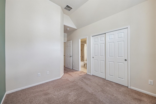 unfurnished bedroom featuring light carpet, connected bathroom, a closet, and lofted ceiling