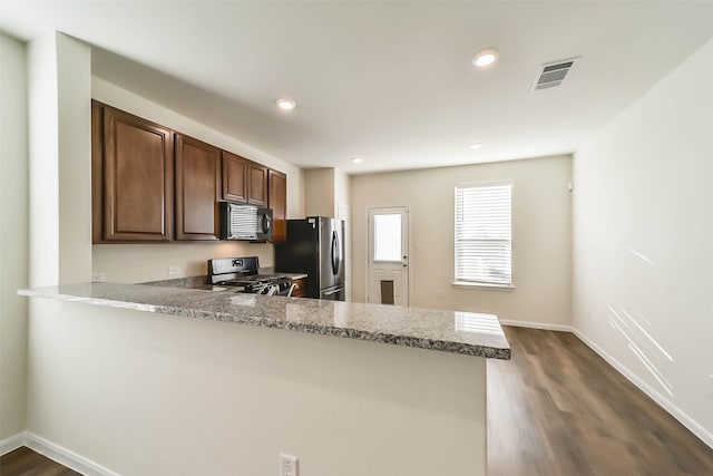 kitchen with dark hardwood / wood-style floors, stainless steel fridge, range with gas stovetop, light stone counters, and kitchen peninsula