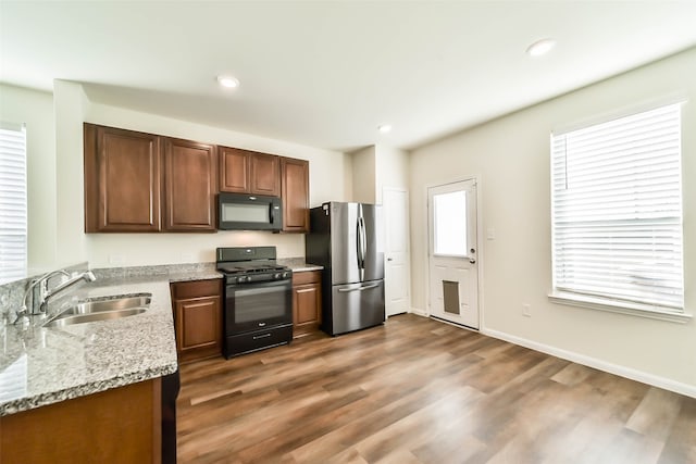 kitchen featuring dark hardwood / wood-style flooring, sink, light stone counters, and black appliances