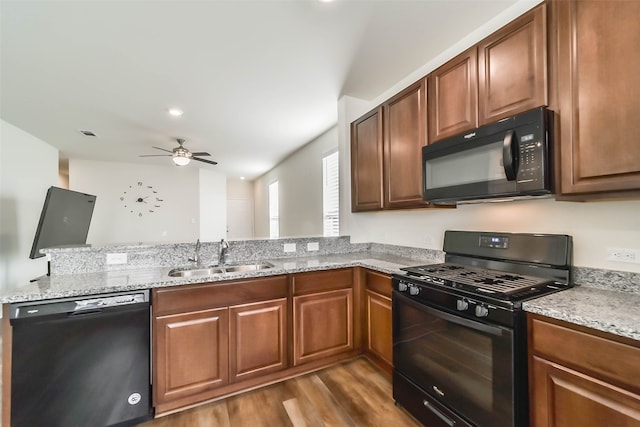 kitchen featuring light stone countertops, sink, ceiling fan, wood-type flooring, and black appliances