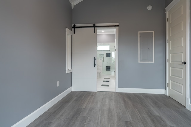 unfurnished bedroom featuring electric panel, crown molding, a barn door, connected bathroom, and wood-type flooring