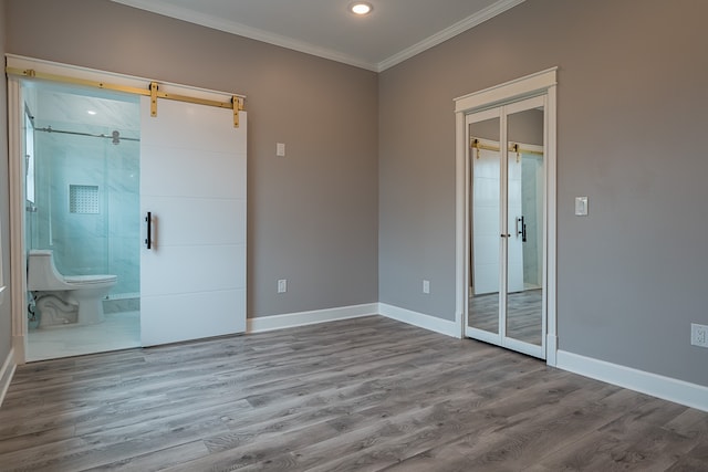 spare room with a barn door, light hardwood / wood-style floors, and ornamental molding