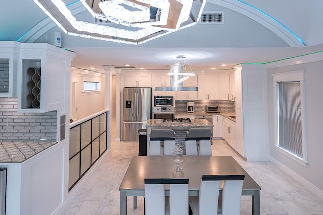 kitchen featuring decorative backsplash, appliances with stainless steel finishes, a kitchen island, pendant lighting, and white cabinetry