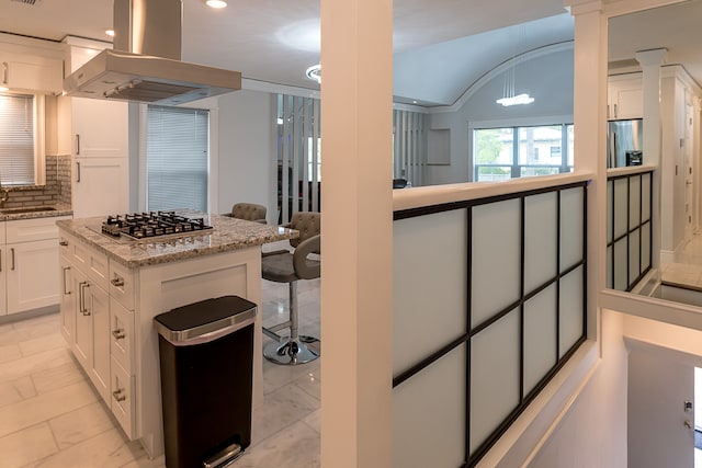 kitchen with island exhaust hood, decorative backsplash, light stone countertops, white cabinetry, and stainless steel gas stovetop