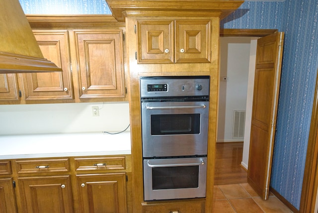 kitchen with custom range hood, stainless steel double oven, and light tile patterned floors