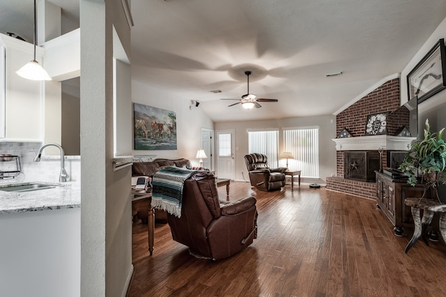 living room with dark hardwood / wood-style flooring, a brick fireplace, vaulted ceiling, ceiling fan, and sink