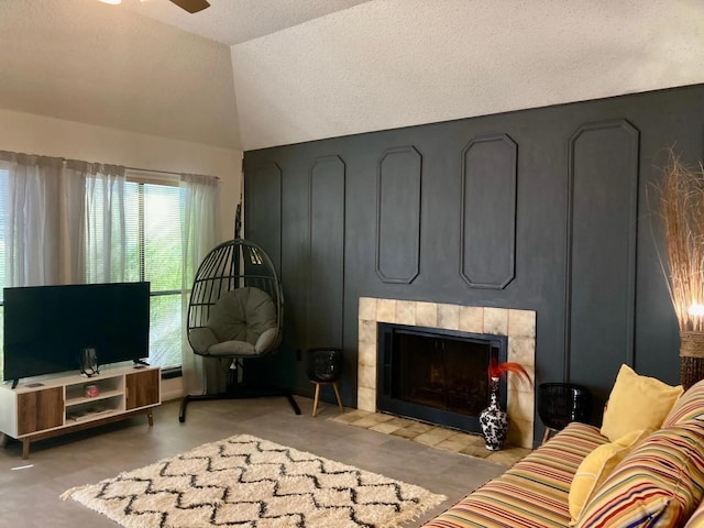 living room featuring a textured ceiling, a tiled fireplace, ceiling fan, and lofted ceiling