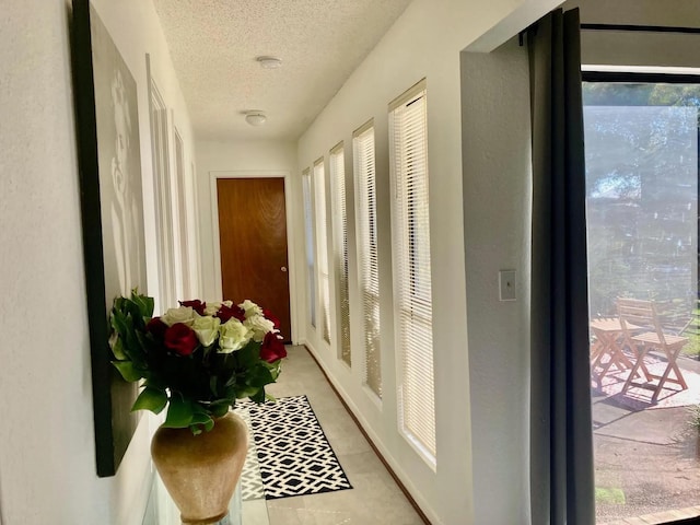 hallway with light tile patterned flooring, a healthy amount of sunlight, and a textured ceiling