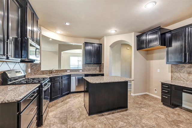 kitchen with a center island, backsplash, sink, light stone countertops, and appliances with stainless steel finishes