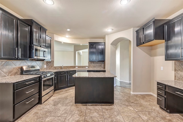 kitchen with light stone countertops, a center island, stainless steel appliances, and backsplash