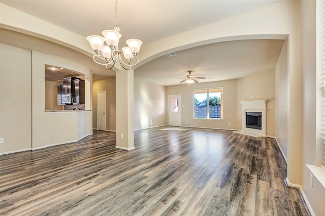 unfurnished living room with ceiling fan with notable chandelier and dark wood-type flooring