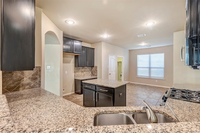 kitchen with decorative backsplash, light stone counters, dark brown cabinets, and sink