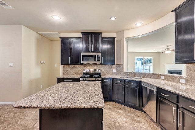 kitchen with backsplash, sink, light stone countertops, a kitchen island, and stainless steel appliances