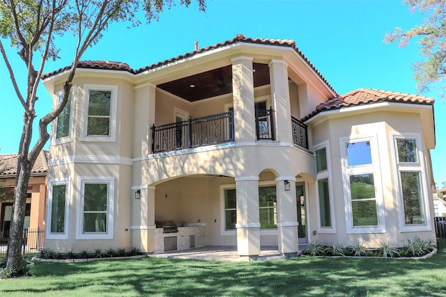 back of property with an outdoor kitchen, a balcony, and a yard