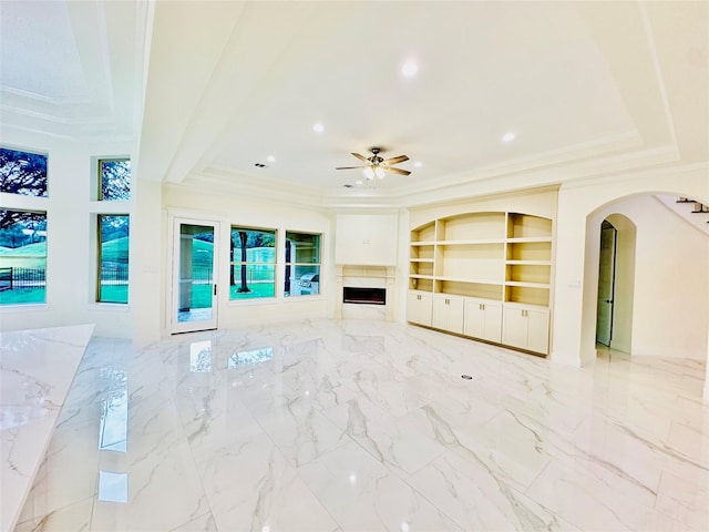 unfurnished living room featuring built in shelves, ceiling fan, and crown molding