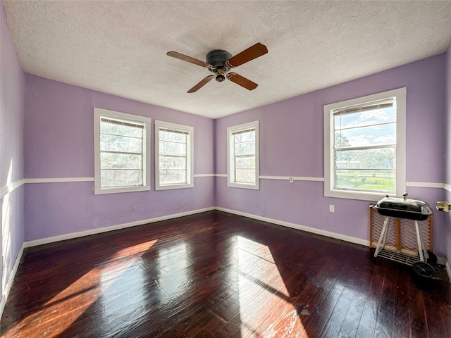 unfurnished room with plenty of natural light, dark hardwood / wood-style floors, a textured ceiling, and ceiling fan