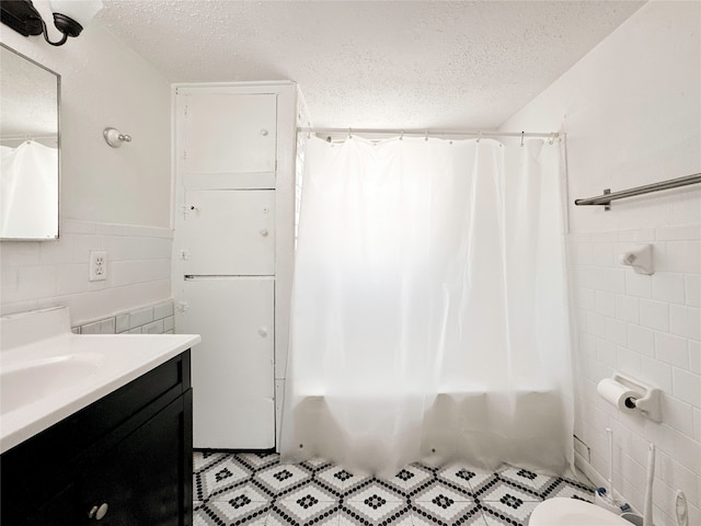 bathroom with a textured ceiling, vanity, shower / tub combo, and tile walls