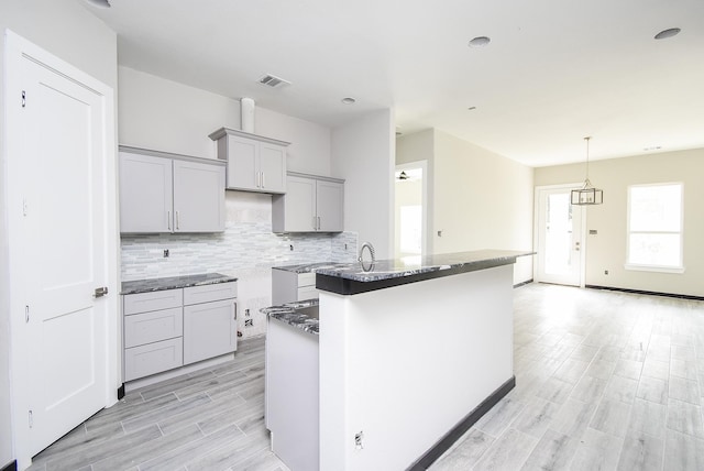 kitchen with gray cabinets, a center island with sink, dark stone counters, and light hardwood / wood-style floors