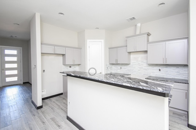 kitchen with backsplash, light hardwood / wood-style floors, a kitchen island with sink, and dark stone counters