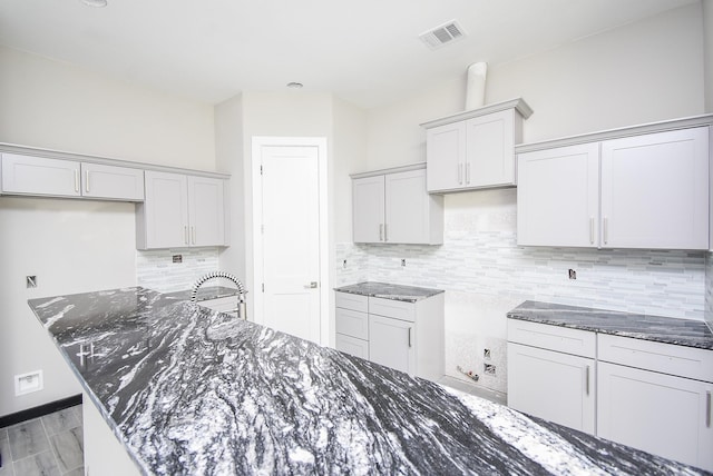 kitchen with a kitchen island, dark stone countertops, light hardwood / wood-style flooring, and tasteful backsplash