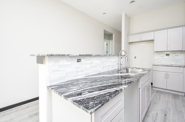 kitchen featuring white cabinetry, sink, light stone counters, light hardwood / wood-style flooring, and decorative backsplash