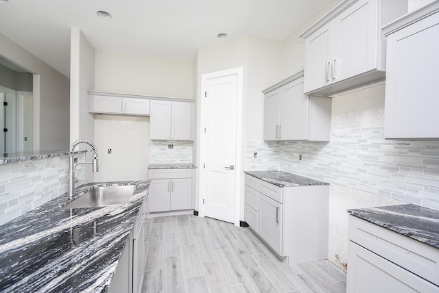 kitchen with sink, backsplash, dark stone countertops, light hardwood / wood-style floors, and white cabinets