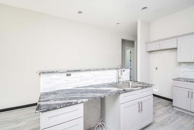 kitchen featuring tasteful backsplash, light hardwood / wood-style flooring, dark stone countertops, and sink