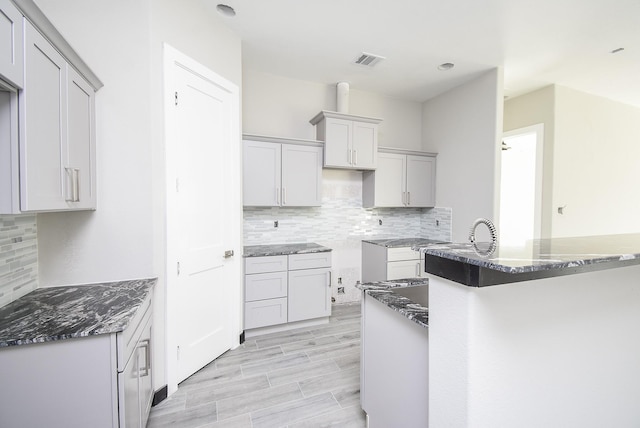 kitchen featuring decorative backsplash, kitchen peninsula, light hardwood / wood-style flooring, and dark stone counters