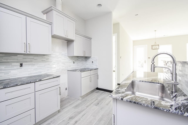 kitchen with backsplash, light hardwood / wood-style flooring, hanging light fixtures, and sink