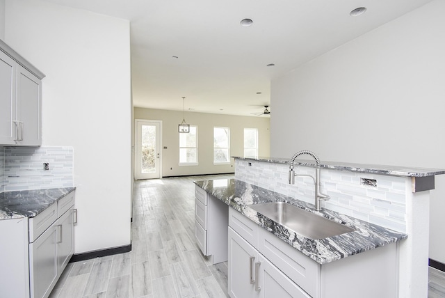 kitchen featuring tasteful backsplash, ceiling fan, sink, stone counters, and light hardwood / wood-style floors