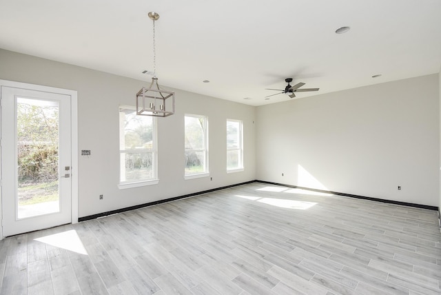 unfurnished dining area with a wealth of natural light, ceiling fan with notable chandelier, and light wood-type flooring