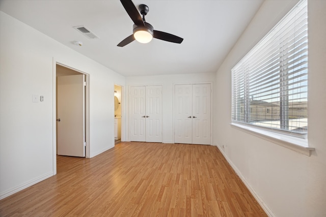 unfurnished bedroom with ceiling fan, light wood-type flooring, and two closets